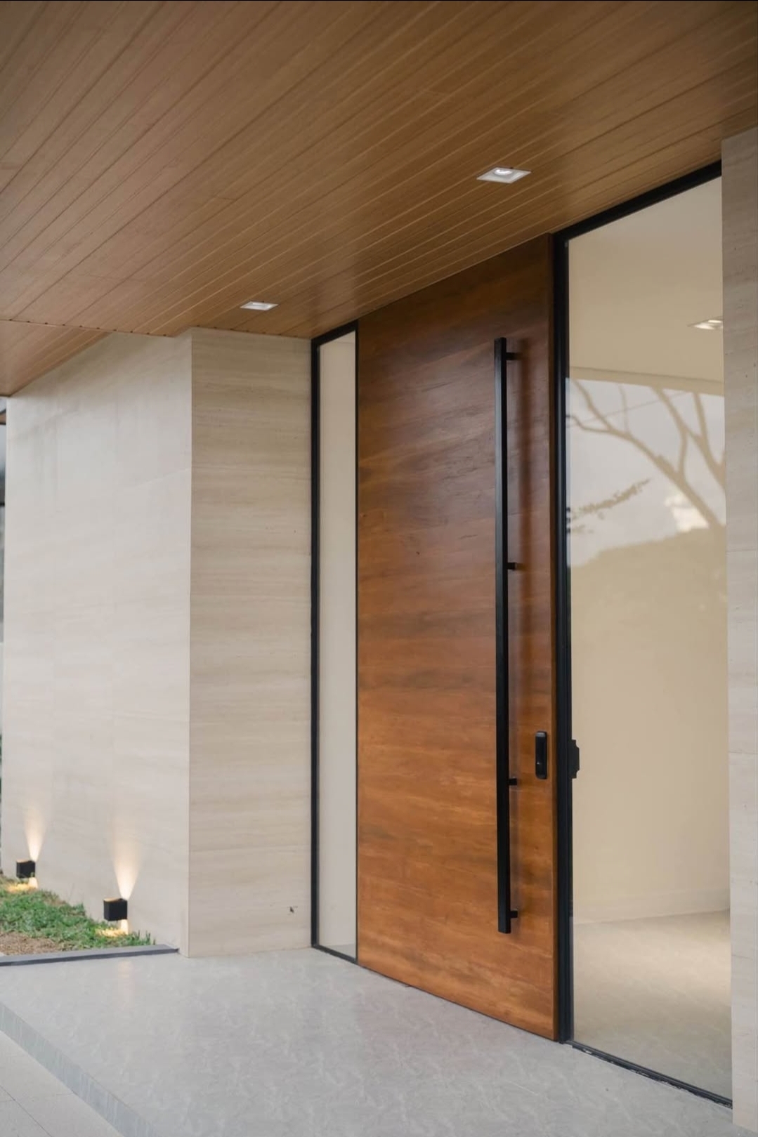 Covered entry with tall timber pivot door and travertine walls
