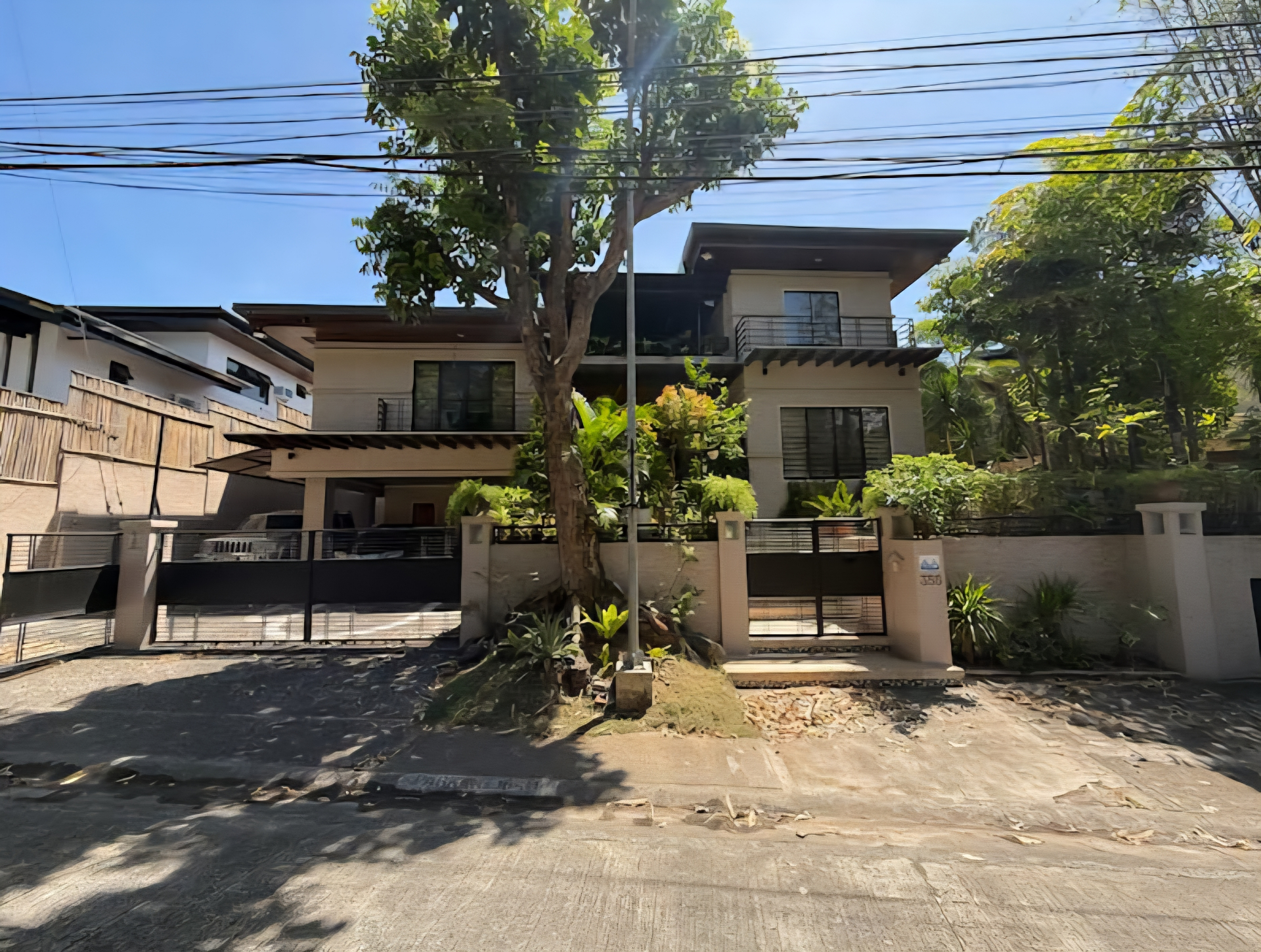 Classic two-storey Ayala Alabang facade behind mature trees and a black steel gate