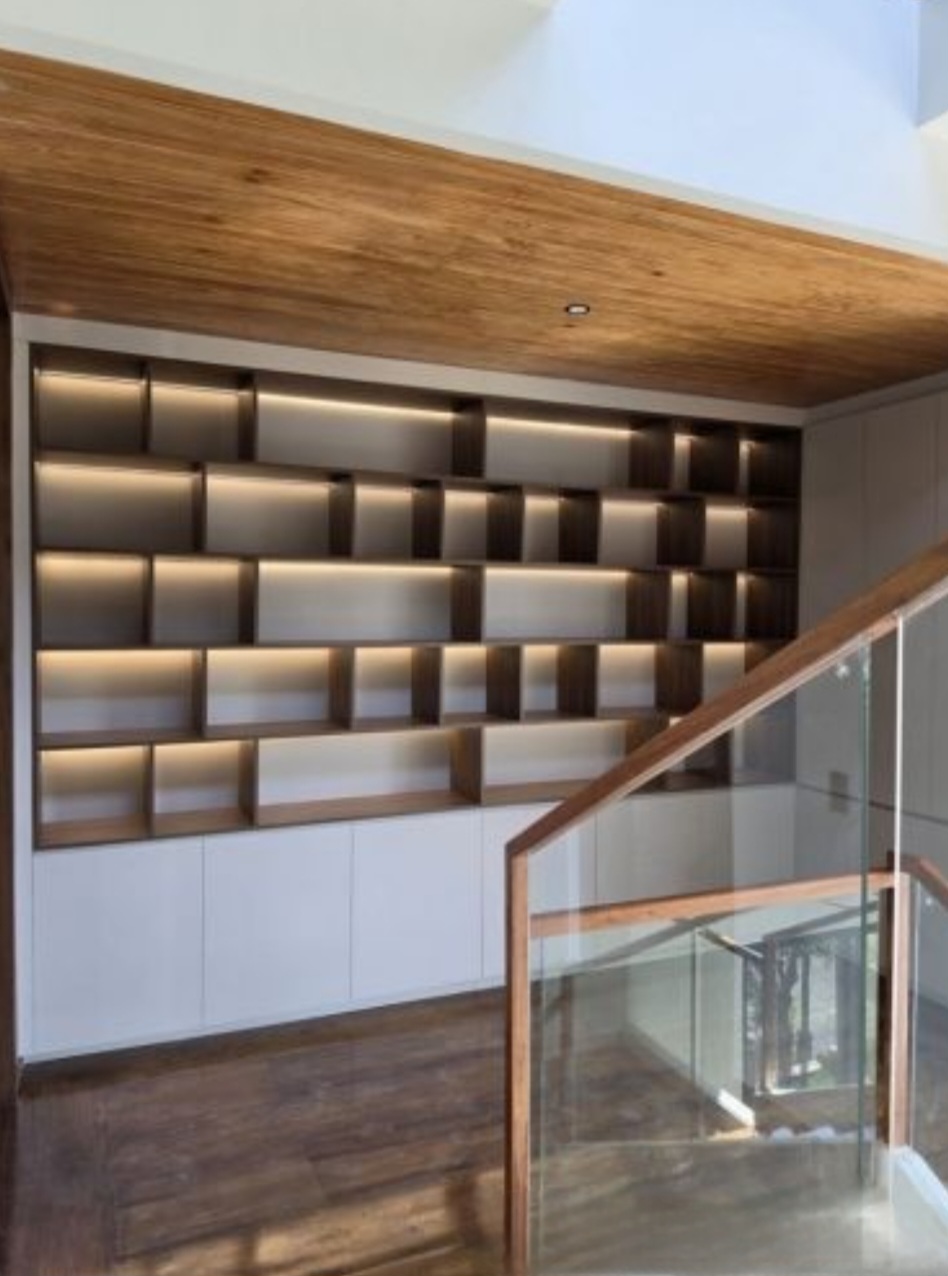 Custom lit built-in shelving wall beside the staircase landing