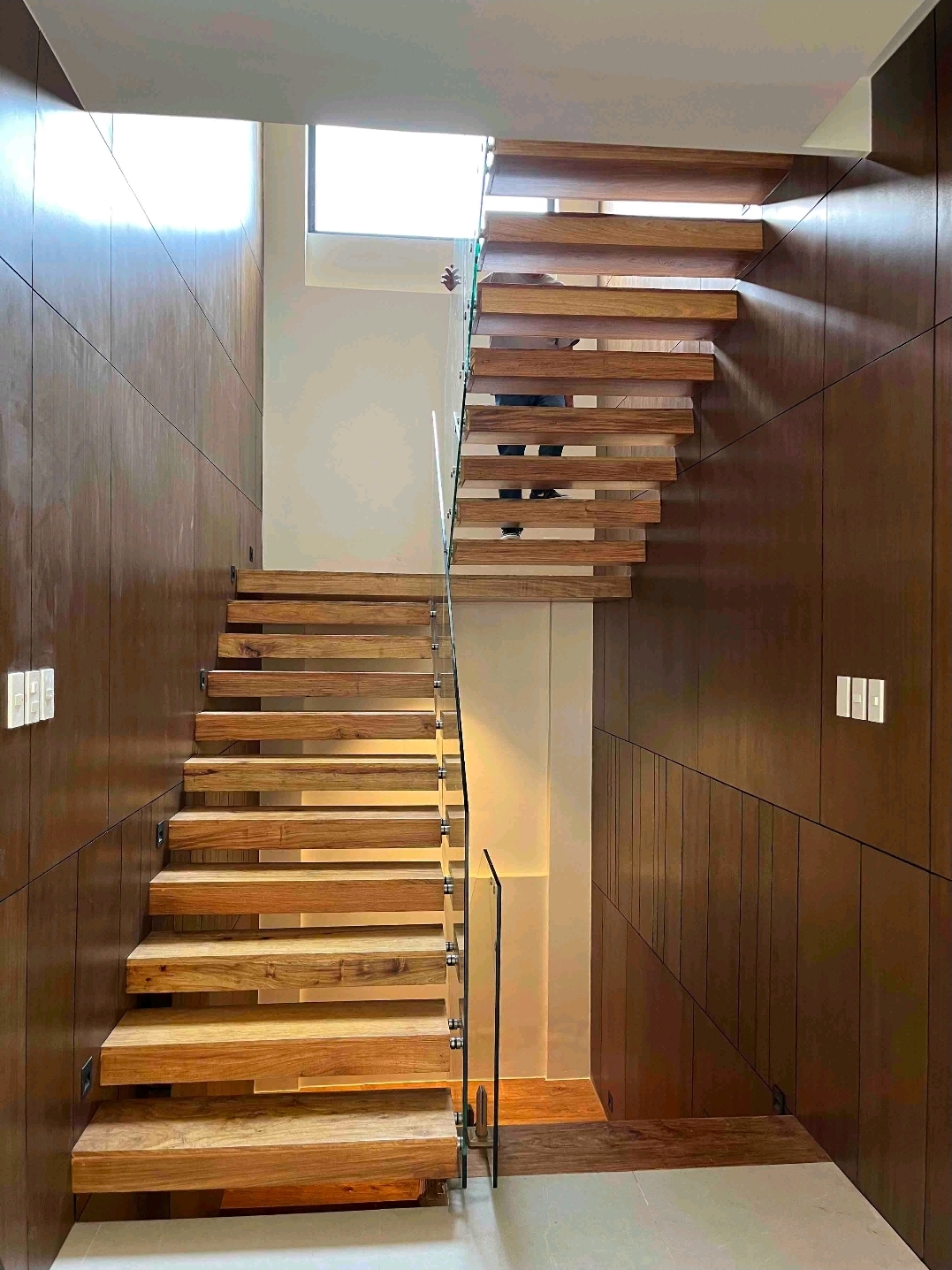 Floating timber staircase with glass balustrade and wood-panelled walls