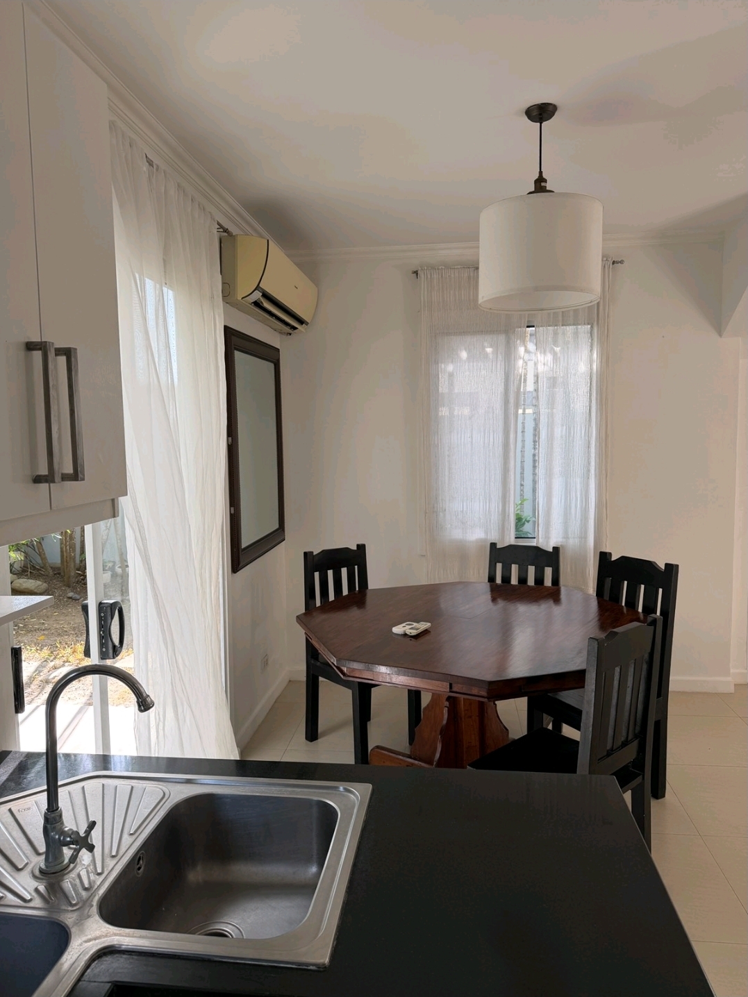 Dining table for four beside the kitchen counter, facing the garden through sheer curtains
