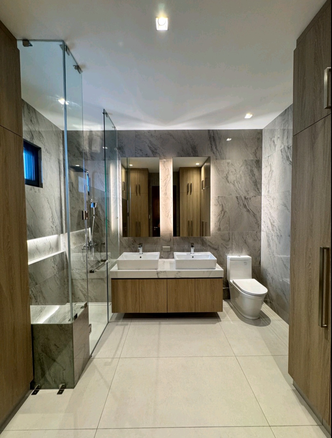 Master bath with marble walls, twin vessel sinks, and glass shower enclosure
