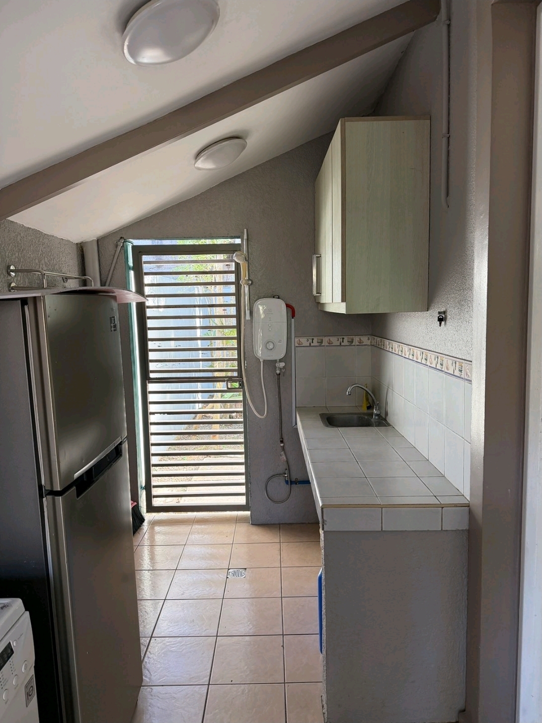 Dirty kitchen and service area with water heater, tiled counter, sink and laundry space