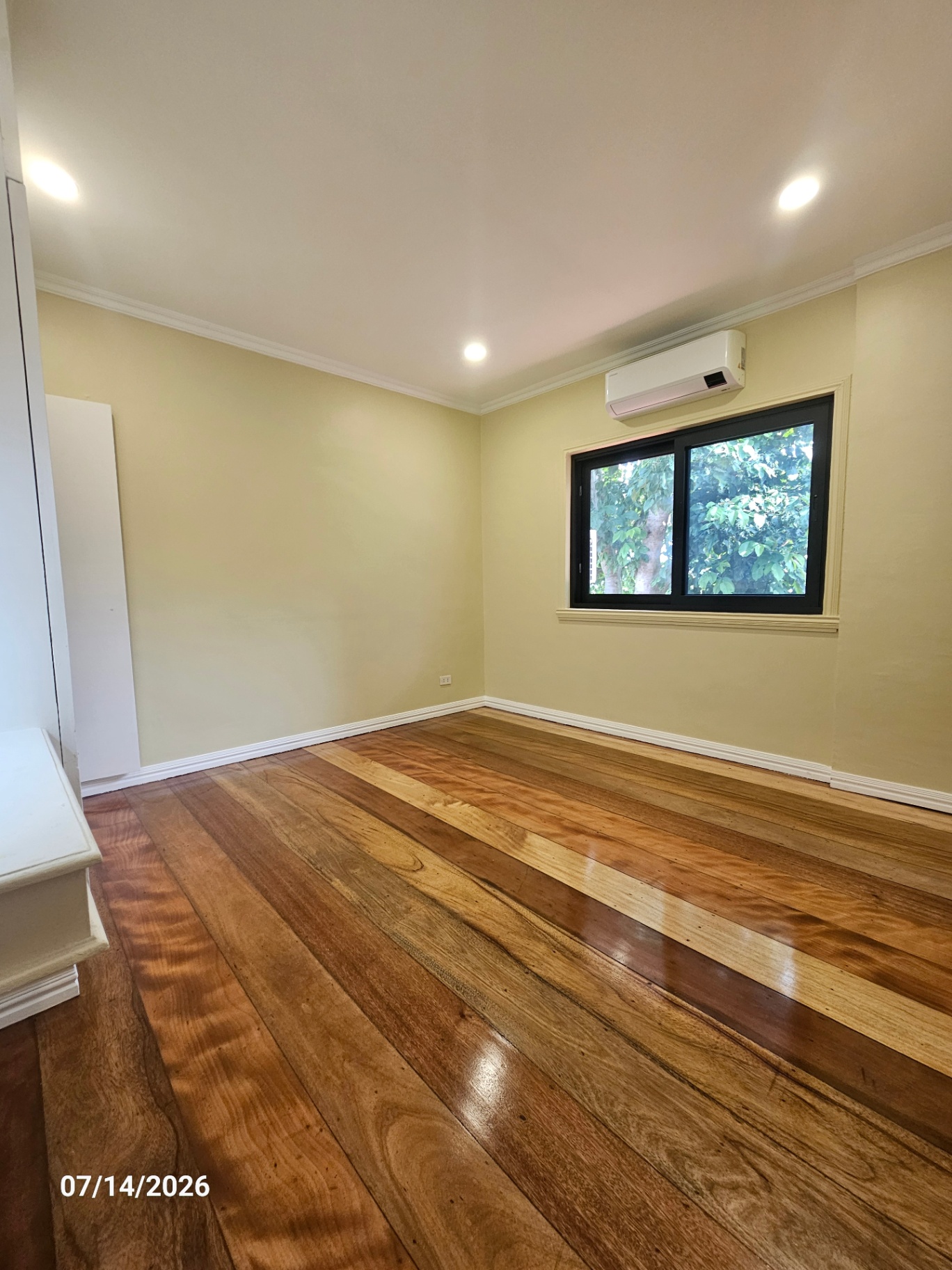 Bright bedroom with butter-yellow walls, hardwood floors, and split-type AC