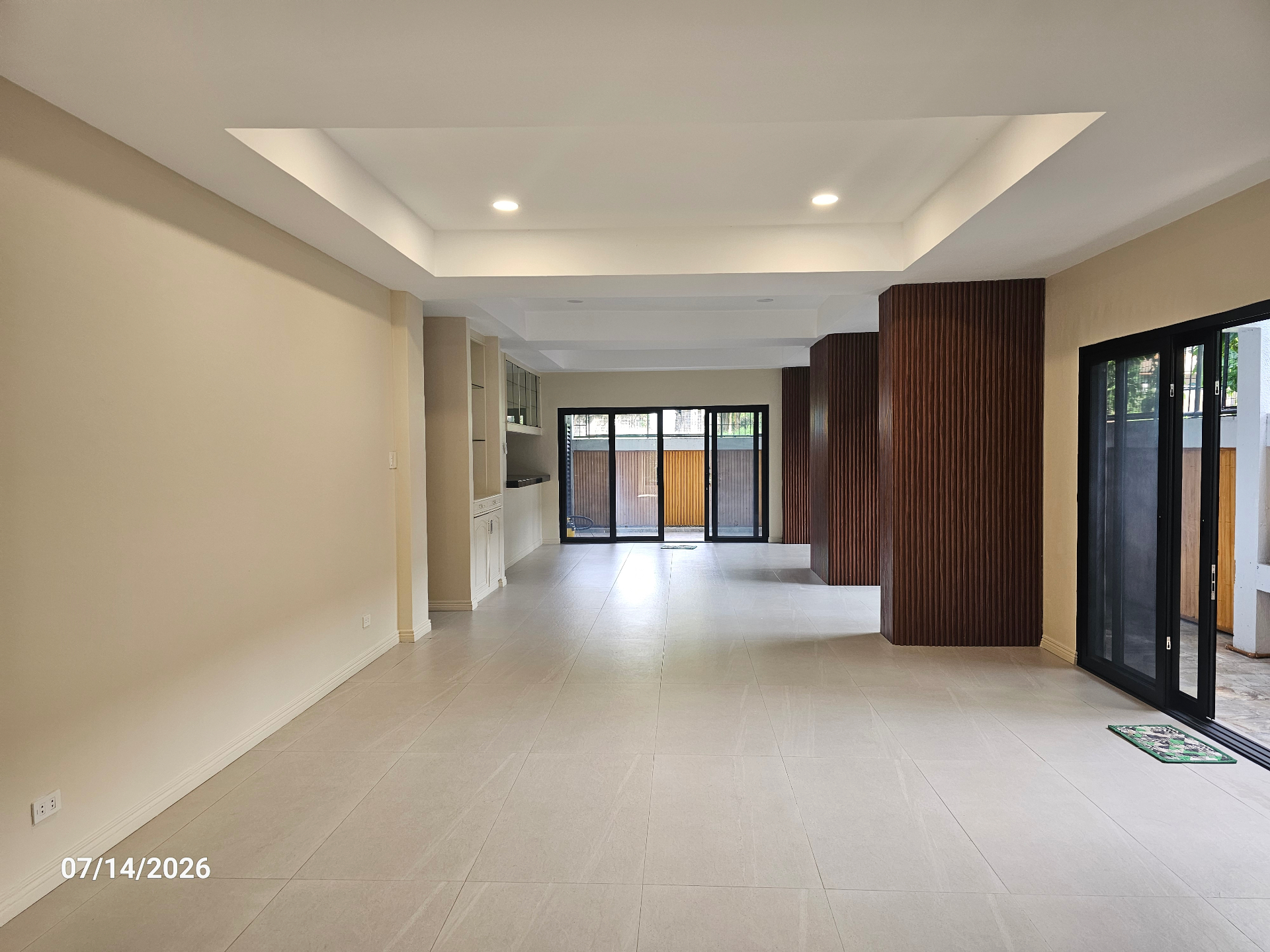 Open-plan great room with tray ceiling, sliding glass doors, and vertical wood-slat feature wall