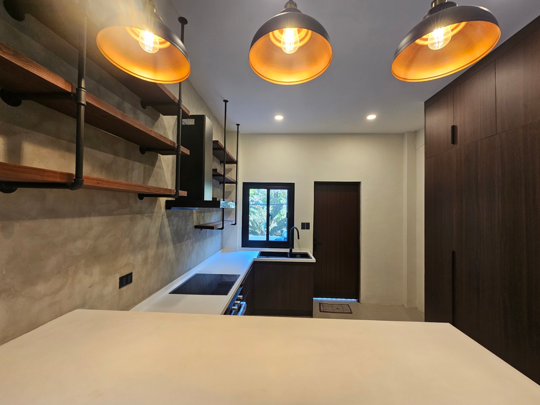 Clean kitchen with industrial pendant lights, pipe-mounted timber shelving and dark cabinetry